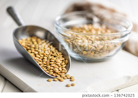 Uncooked green lentil in scoop on white table. Uncooked green lentil in scoop on white table. 136742025