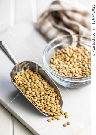 Uncooked green lentil in scoop on white table. Uncooked green lentil in scoop on white table. 136742026