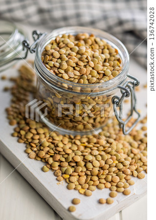 Uncooked green lentil in jar on white table. Uncooked green lentil in jar on white table. 136742028
