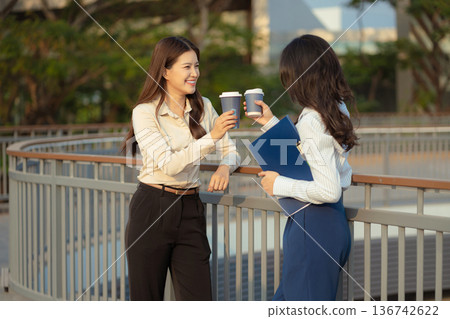 Female colleague asian descent holds a cup of coffee and talking discussion ideas and happily. Female colleague asian descent holds a cup of coffee and talking discussion ideas and happily. 136742622