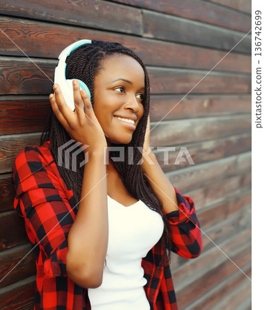 Portrait happy modern African young woman listening to music with headphones Portrait happy modern African young woman listening to music with headphones 136742699