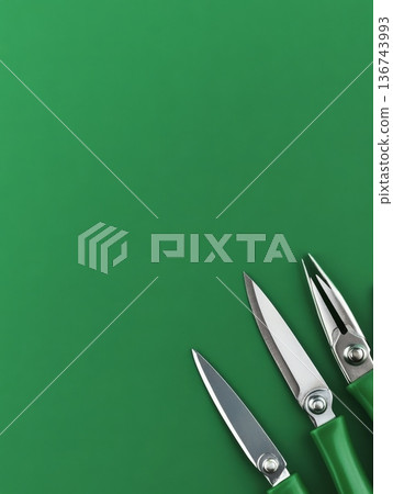 Three silver scissors with green handles placed in the corner of a vibrant green background, offering ample copy space for design or text 136743993