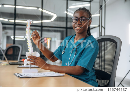 Detailed explanation of human spine model. Female doctor in coat is in the office clinic 136744587