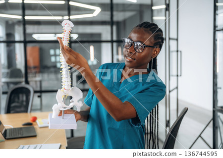Teaching the bone structure in spine model. Female doctor in coat is in the office clinic 136744595