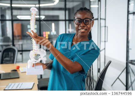 Teaching the bone structure in spine model. Female doctor in coat is in the office clinic 136744596