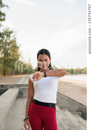 Fit Asian Woman in Sportswear Standing Outdoors in Park Environment Using Smartwatch Fit Asian Woman in Sportswear Standing Outdoors in Park Environment Using Smartwatch 136744767
