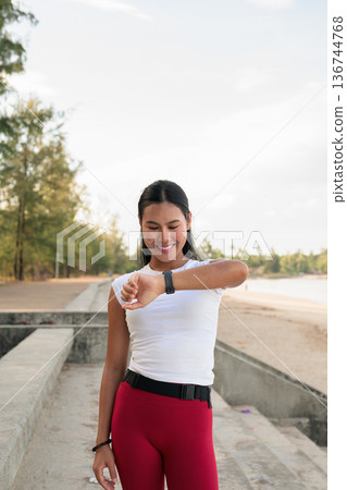 Fit Asian Woman in Sportswear Standing Outdoors in Park Environment Using Smartwatch Fit Asian Woman in Sportswear Standing Outdoors in Park Environment Using Smartwatch 136744768