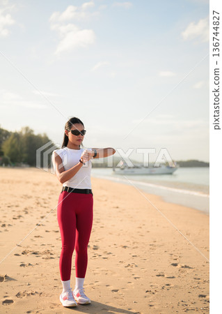 Fit Asian Woman in Sportswear Standing on Beach During Summer Workout Using Smart Watch Fit Asian Woman in Sportswear Standing on Beach During Summer Workout Using Smart Watch 136744827