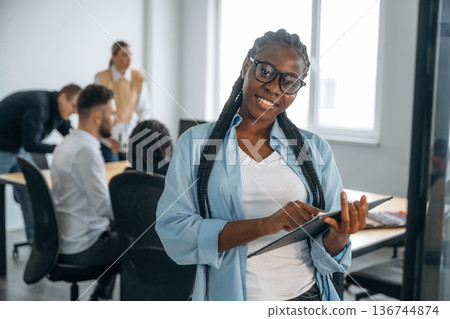 Woman is standing and smiling. Business people are working in the office Woman is standing and smiling. Business people are working in the office 136744874