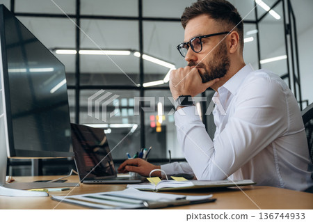 View from the side. Business person is sitting by computer in office and working View from the side. Business person is sitting by computer in office and working 136744933
