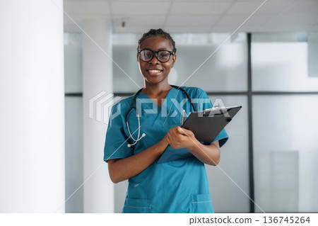Black notepad in hands. Female doctor is indoors in modern room 136745264