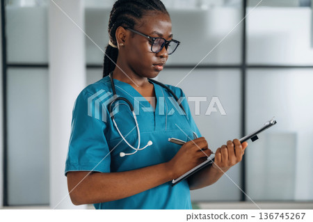 Writing information into documents. Female doctor is indoors in modern room Writing information into documents. Female doctor is indoors in modern room 136745267