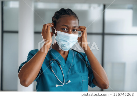 Wearing the mask. Female doctor is indoors in modern room Wearing the mask. Female doctor is indoors in modern room 136745268