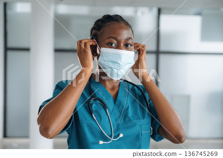 Wearing the mask. Female doctor is indoors in modern room 136745269