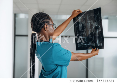 Examining the x-ray. Female doctor is indoors in modern room Examining the x-ray. Female doctor is indoors in modern room 136745284