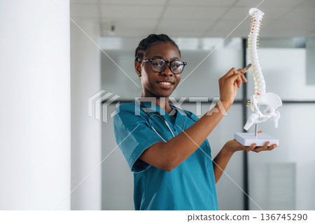 Human spine model, teaching and showing. Female doctor is indoors in modern room 136745290