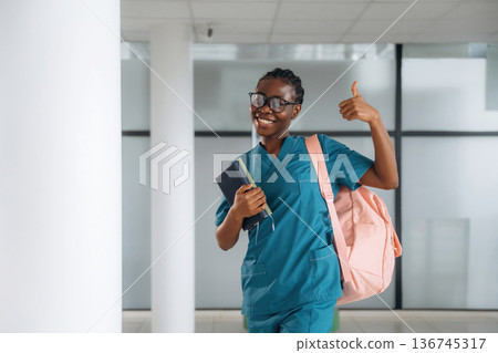 Thumb up, smiling. Woman student with pink backpack is indoors Thumb up, smiling. Woman student with pink backpack is indoors 136745317