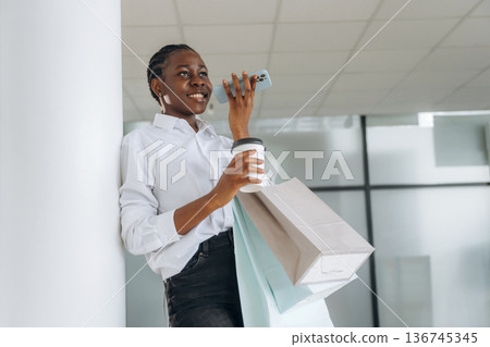 Cup of drink, shopping bags and phone. Businesswoman in formal clothes is in the modern room Cup of drink, shopping bags and phone. Businesswoman in formal clothes is in the modern room 136745345