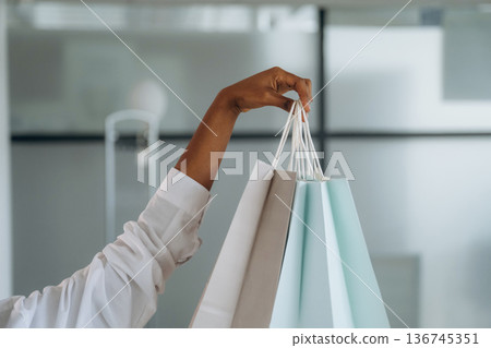 Close up view of woman's hand that is holding shopping bags indoors Close up view of woman's hand that is holding shopping bags indoors 136745351