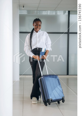 Suitcase is on the floor, ready for vacation. Businesswoman in formal clothes is in the modern room Suitcase is on the floor, ready for vacation. Businesswoman in formal clothes is in the modern room 136745390