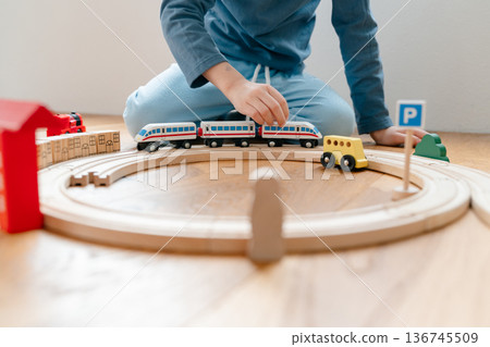 Toddler playing with wooden train railway on floor at home. Cozy indoor family activity in modern apartment, natural light, early childhood bonding and mindful parenting concept 136745509