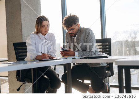 Cooperation, working on project. Man and woman are indoors in modern building Cooperation, working on project. Man and woman are indoors in modern building 136745610