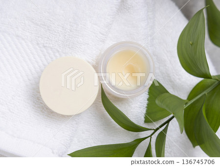 Opened balm jar with natural herbal salve on white towel near green leaves, skincare product Opened balm jar with natural herbal salve on white towel near green leaves, skincare product 136745706