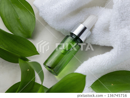 Glass dropper bottle near white bath towel and green leaves, skincare serum packaging mockup Glass dropper bottle near white bath towel and green leaves, skincare serum packaging mockup 136745716