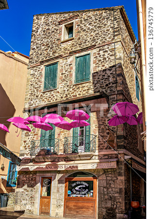 Collioure, France - Nov 03, 2025: Pink umbrellas hanging in the streets of Collioure in France. 136745779