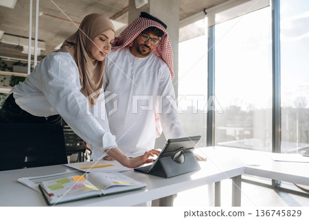 In traditional clothes. Muslim man and woman are indoors in modern building In traditional clothes. Muslim man and woman are indoors in modern building 136745829