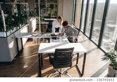 Illuminated by sunlight. Man and woman are indoors in modern building Illuminated by sunlight. Man and woman are indoors in modern building 136745853