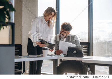 Digital tablet and documents. Man and woman are indoors in modern building Digital tablet and documents. Man and woman are indoors in modern building 136745861