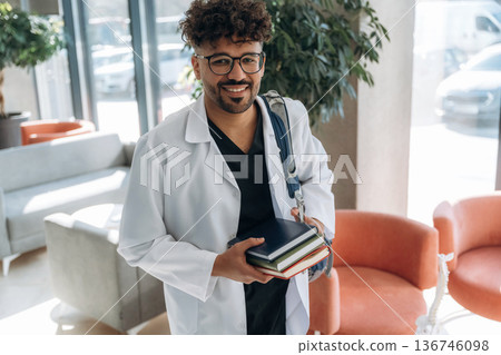 Bunch of books in hands. Man is indoors in the modern building 136746098