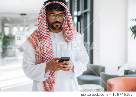 Holding smartphone. Arab businessman is in the office 136746102