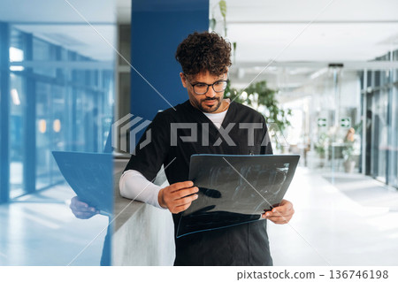 Examining the x-ray. Male doctor is indoors in the modern building Examining the x-ray. Male doctor is indoors in the modern building 136746198