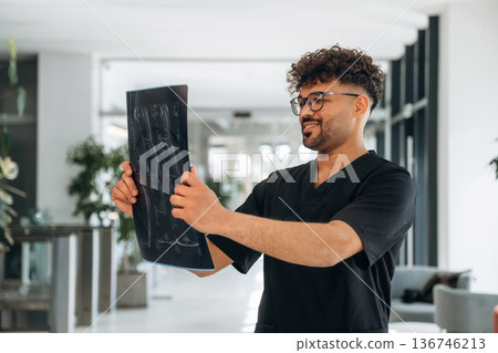 Examining the x-ray. Male doctor is indoors in the modern building Examining the x-ray. Male doctor is indoors in the modern building 136746213