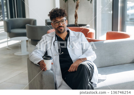 Holding paper cup of drink, break. Doctor is indoors in the modern building Holding paper cup of drink, break. Doctor is indoors in the modern building 136746254