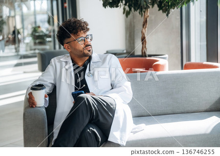 Holding paper cup of drink, break. Doctor is indoors in the modern building Holding paper cup of drink, break. Doctor is indoors in the modern building 136746255