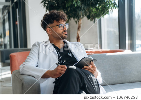 On sofa, with notepad. Doctor is indoors in the modern building 136746258