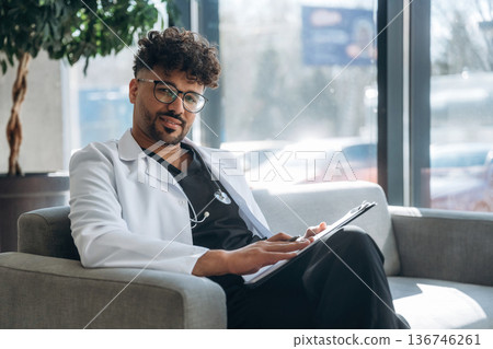 On sofa, with notepad. Doctor is indoors in the modern building 136746261