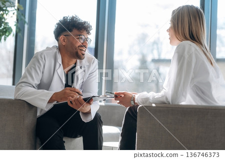 Sitting and talking. Man and woman are indoors in modern building Sitting and talking. Man and woman are indoors in modern building 136746373
