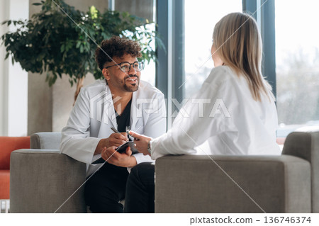 Sitting and talking. Man and woman are indoors in modern building Sitting and talking. Man and woman are indoors in modern building 136746374