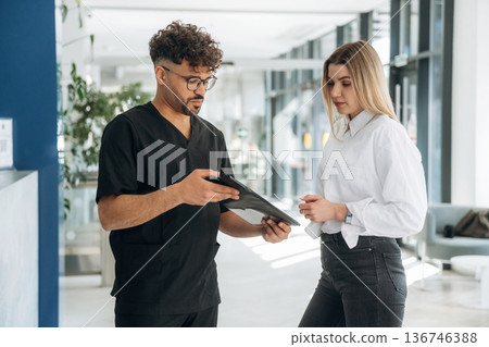 Showing information in notepad. Man and woman are indoors in modern building Showing information in notepad. Man and woman are indoors in modern building 136746388