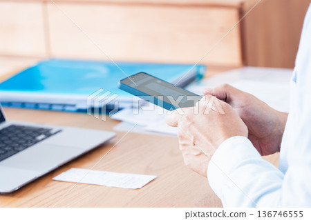 一名男子正在使用電腦和智慧型手機準備報稅表。 136746555