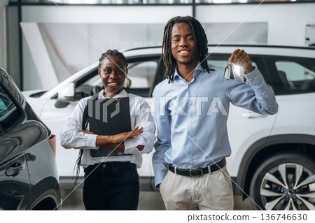 Happy owner is holding keys. Car seller is assisting client in the automobile salon 136746630