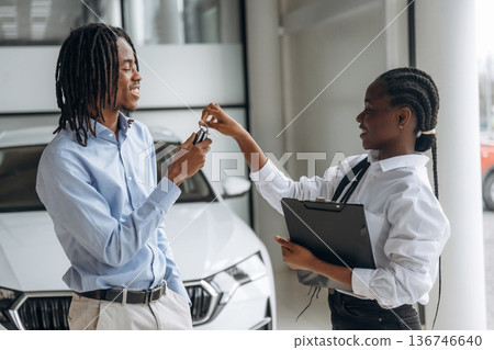 Taking keys, happy owner. Car seller is assisting client in the automobile salon Taking keys, happy owner. Car seller is assisting client in the automobile salon 136746640