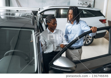 Doors are opened, looking inside. Car seller is assisting client in the automobile salon Doors are opened, looking inside. Car seller is assisting client in the automobile salon 136746646