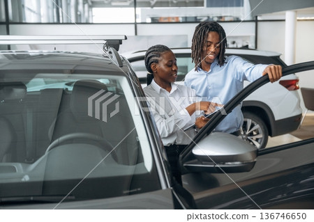 Documents in hands. Car seller is assisting client in the automobile salon Documents in hands. Car seller is assisting client in the automobile salon 136746650