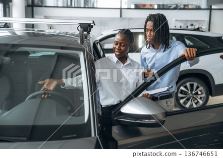 Looking at black vehicle. Car seller is assisting client in the automobile salon Looking at black vehicle. Car seller is assisting client in the automobile salon 136746651