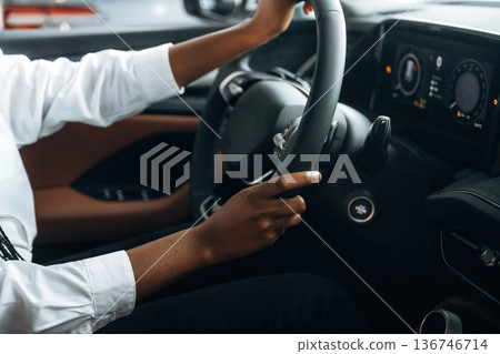 Two hands are on the steering wheel. Woman in white shirt is in the modern car 136746714
